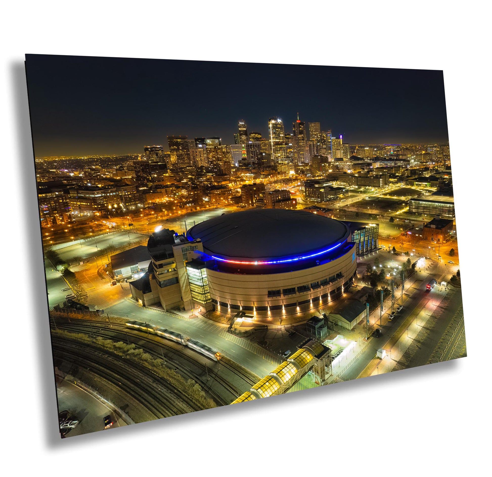 Nighttime aerial view of a city skyline with a large illuminated arena. The arena has a domed roof with blue and red lighting.  The city features skyscrapers and urban infrastructure. The image showcases a metal print of an urban landscape at night, ideal for home or office decor. The print features vibrant colors and sharp details, capturing the city&#39;s energy and the arena&#39;s architectural design. The overall aesthetic is modern and sophisticated.