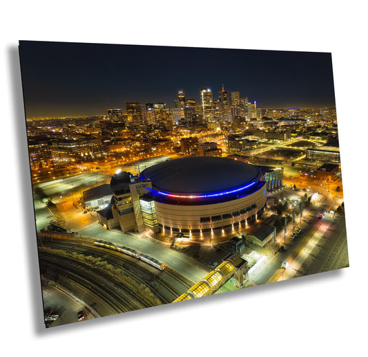 Nighttime aerial view of a city skyline with a large illuminated arena. The arena has a domed roof with blue and red lighting.  The city features skyscrapers and urban infrastructure. The image showcases a metal print of an urban landscape at night, ideal for home or office decor. The print features vibrant colors and sharp details, capturing the city&#39;s energy and the arena&#39;s architectural design. The overall aesthetic is modern and sophisticated.